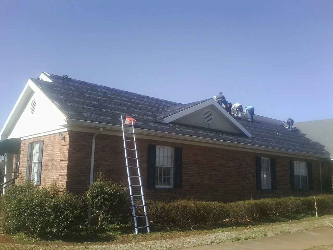 Crew tearing shingles off a brick ranch roof with a ladder set — Emergency Roof Repair work by our crew in Larue