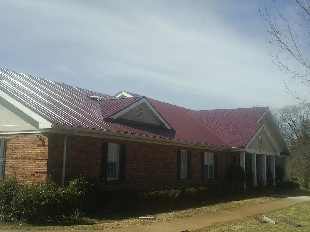 Red metal roof with gabled entries on a long brick building, from a Hail Damage Roof Repair job in Larue