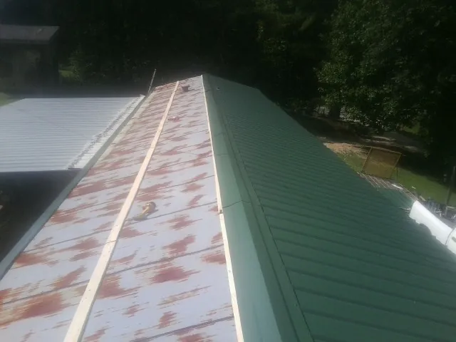 Old rusted panels beside newly installed green metal roofing — Wind Damage Roof Repair by Roofing Brothers in Larue