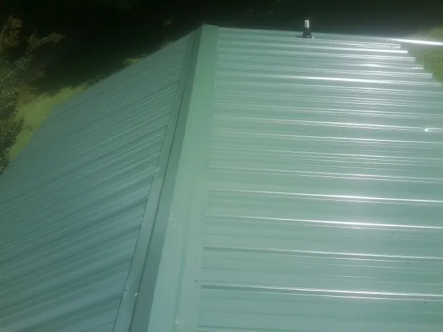 New green metal panels meeting at the ridge of a roof — Flat Roof Repair work by our crew in Larue