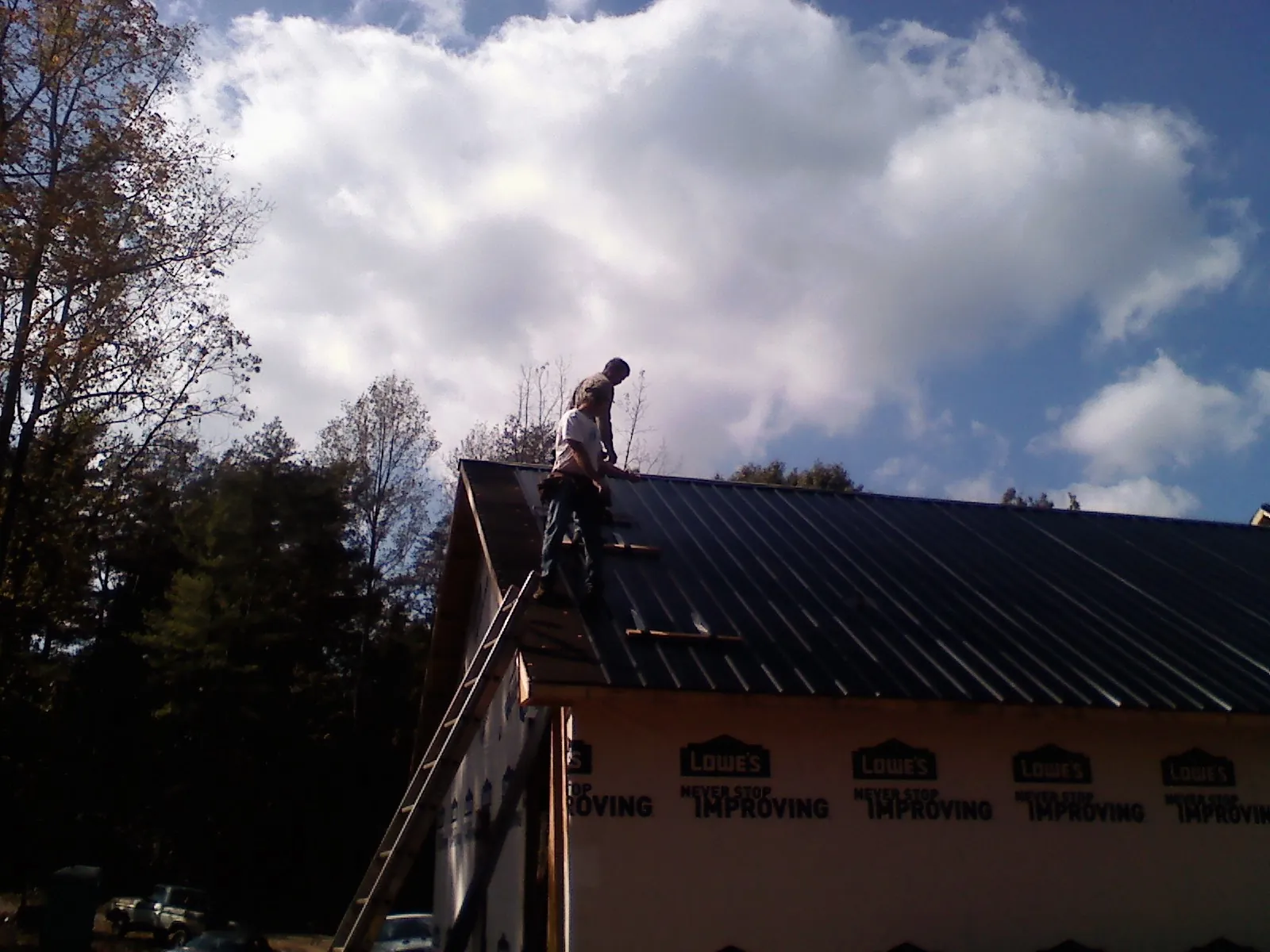Roofer fastening dark metal panels high against a cloudy sky, from a Roof Inspection job in Larue