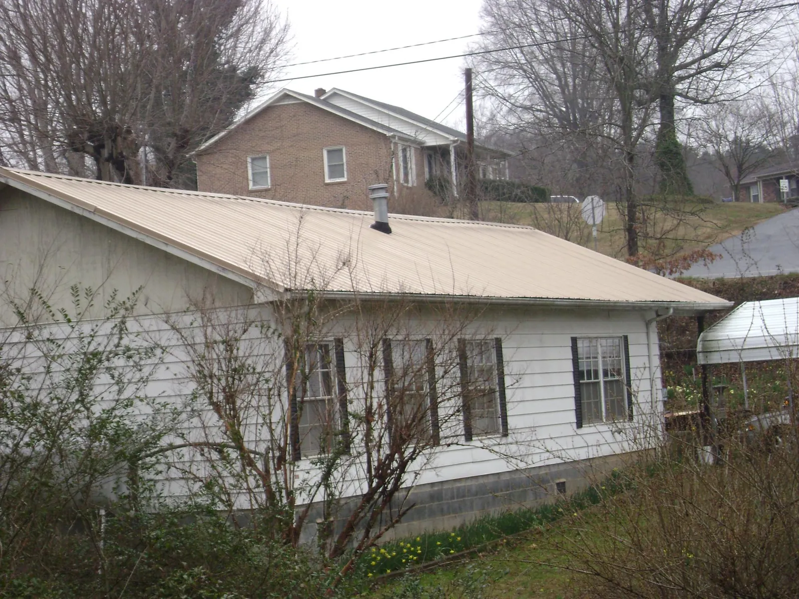 Tan metal roof on a white sided house set into a hillside — Commercial Roofing by Roofing Brothers in Larue