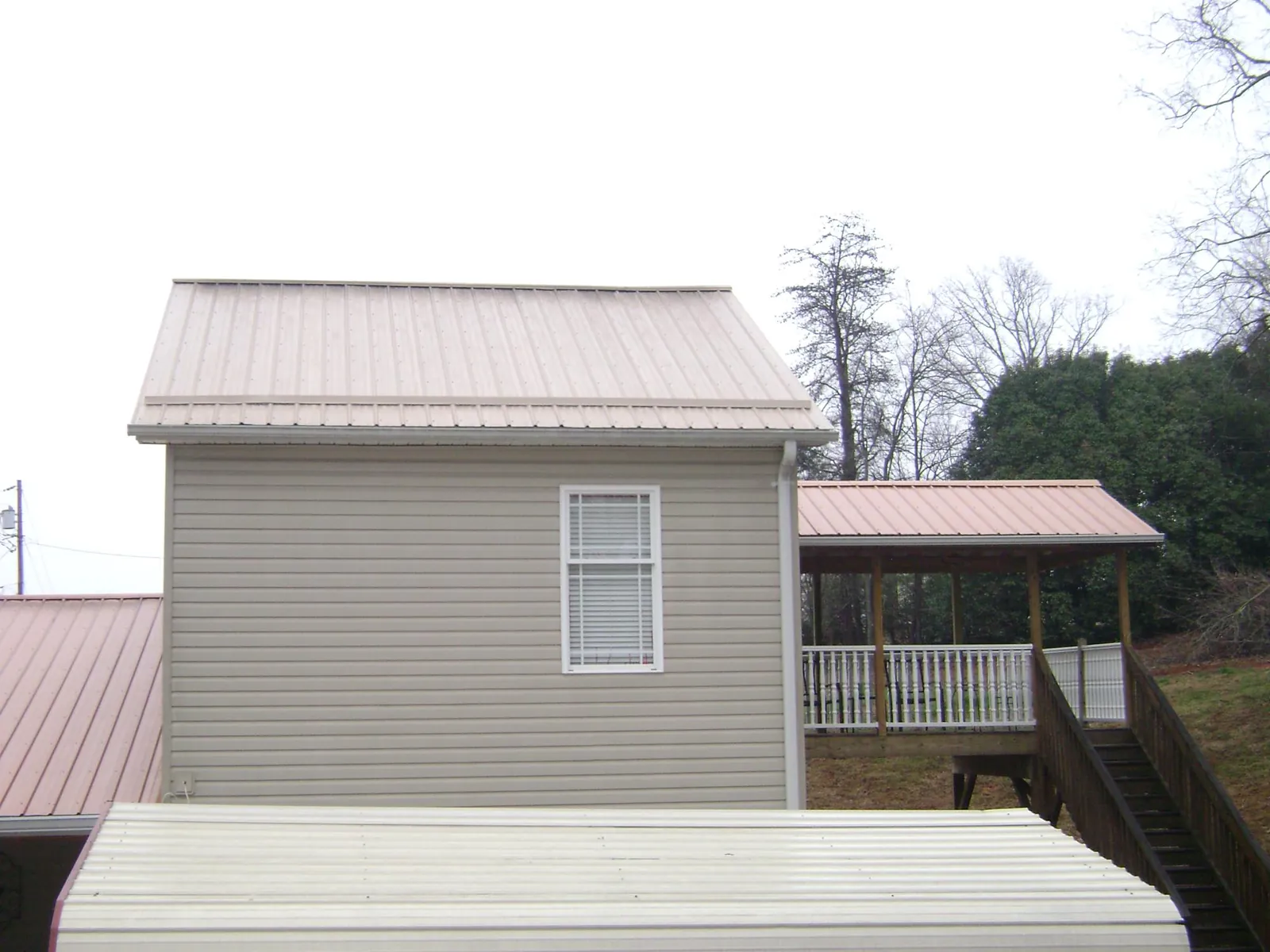 Tan metal roofs on a two story addition and attached porch, from a Roof Replacement job in Larue